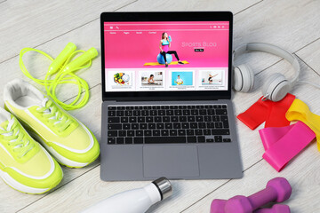 Laptop with sport blog web site and different gym stuff on floor, above view