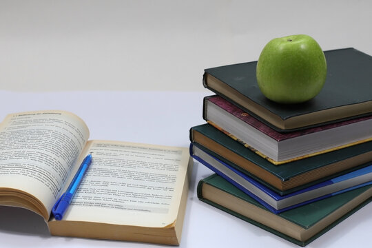 Stack of Books with Green Apple and Open Notebook with Pen on Beige Background