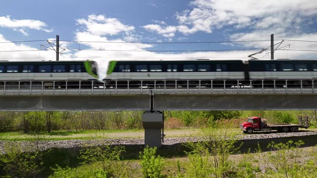 Camera pans up from lush greenery to a blue sky as the REM train speeds across an elevated railway track in Montreal.