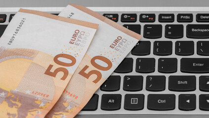 Euro banknotes lying on a computer keyboard, close-up