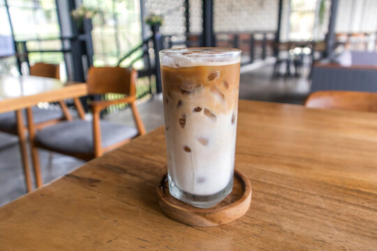 Iced coffee latte in a tall glass with milk on a blur cafe background. Summer refreshment concept. Front view.