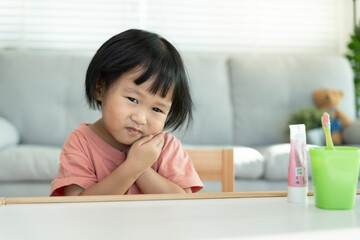 Fototapeta premium little asian girl presses hand to cheek, suffers from pain in tooth. Teeth decay, dental problems, child emotions and facial expression, oral health care, reducing sweets, fluorine coating