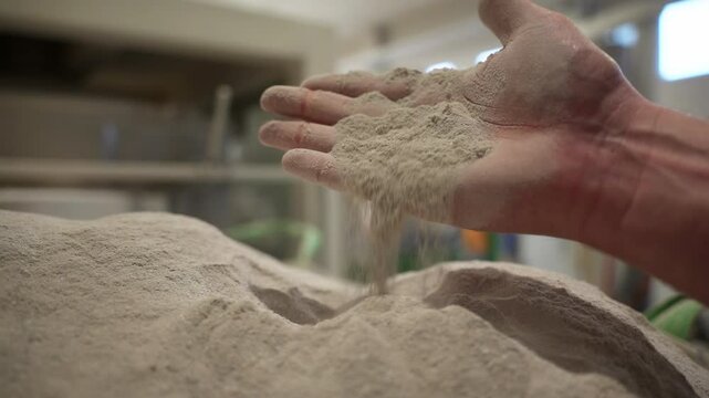 Worker hand takes and pours out dry powder in chemical fertilizers manufacturing workshop. Employee checks material for production in warehouse closeup