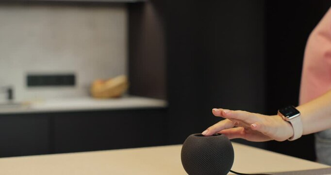 Smart speaker activates in a kitchen environment. Woman turns on smart speaker that activates artificial intelligence assistant.