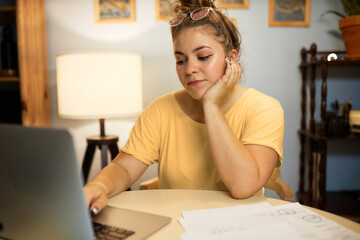 Indoor image of bored caucasian female freelancer procrastinating sitting at table in front of laptop and documents, scrolling, avoiding starting new project or finishing her work in time