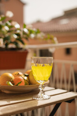 A glass with Italian lemon liqueur and a plate of fresh citrus fruits on the table on the sunny balcony.