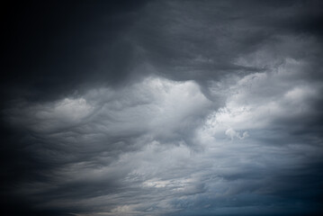 The photo shows a dark stormy sky with dense clouds. Faint light breaks through the thick cloud cover, creating a contrast between the bright and dark areas of the sky.