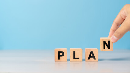 Close-up of hand holding a wooden block with the word PLAN. Symbol of strategy, vision, and organization in business.