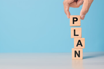 hand shows wooden block with PLAN letters. Represents goal setting, business development, and management process.