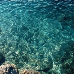 Obraz premium Crystal Clear Turquoise Water with Sunlight Reflections and Coastal Rocks
