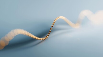 Naklejka premium Close-up of a single strand of gold beads on a blue background. the beads are arranged in a curved line, creating a wave-like pattern.