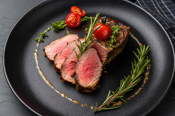Slice of roast beef garnished with herbs and tomato on a luxurious black plate, top view