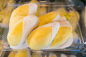 Close-up of durian fruit neatly packed in a clear plastic container, showcasing bright yellow flesh and white edible seeds