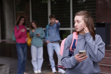 Teenage girl with smartphone suffering from bullying at school, selective focus