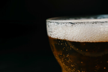 Refreshing golden beer with foam and bubbles in a glass, isolated on a dark background