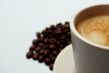 Freshly brewed coffee in a white cup sits on a saucer with roasted coffee beans scattered nearby, creating a cozy and inviting scene