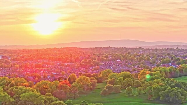 Aerial: fire sky sunset over Heaton Park with forest and trees in Prestwich, Manchester, England, crane up drone shot