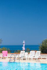 Obraz premium Swimming pool overlooking the sea with sunbeds and parasol on a sunny day