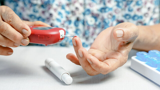 Elderly person using blood glucose meter to check blood sugar level at home, diabetes management, health care, and self monitoring concept.