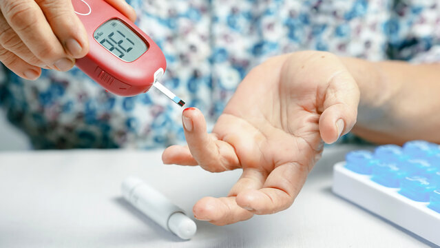 Blood glucose meter diabetes test finger prick elderly hand medical device healthcare monitoring close up chronic illness self care. An elderly person checks blood sugar level home showing self.