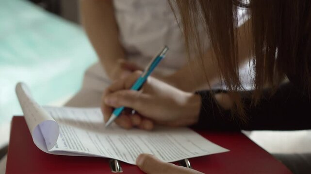 Woman client signing insurance and consent form at clinic. Patient filling medical documentation before aesthetic treatment. Female completing health agreement paperwork in cosmetic office
