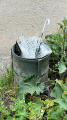 discarded broken umbrella thrown away into outdoor trash can or garbage bin