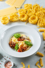 Delicious spaghetti bolognese with basil and parmesan, surrounded by various types of pasta