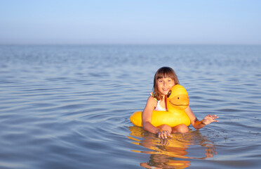 Child playing in calm water with inflatable duck under blue sky