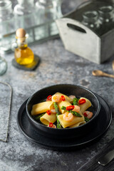 Paccheri pasta with shrimps, asparagus and chili pepper resting on a dark plate