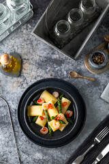 Paccheri pasta with shrimps, asparagus and chili pepper on a dark plate
