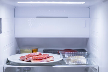 Raw meat storing in refrigerator, plate with beef steaks and chicken breast in plastic container