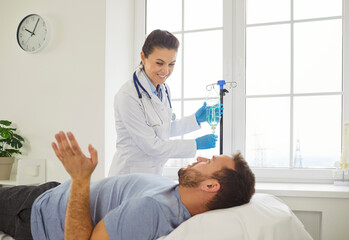 Man with intravenous drip on medical couch, physician, nurse fixing IV drip infusion for hospital...
