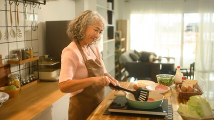 An Elderly Asian Woman Cooking Breakfast in a Bright Home Kitchen, Concept Senior domestic lifestyle
