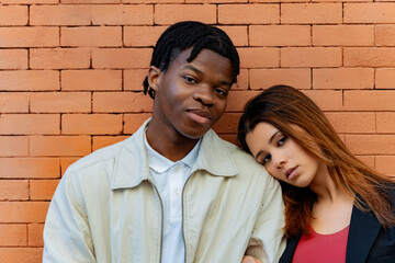 Interracial couple posing together with woman leaning her head on man's shoulder in front of a...