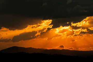 Golden sunset with dramatic clouds and sun rays over mountain hills. Warm evening light creates a breathtaking natural landscape full of depth, color, and peaceful atmosphere