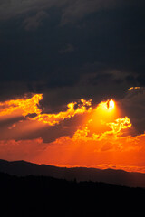 Golden sunset with dramatic clouds and sunlight rays over mountain hills. Warm glowing light creates a breathtaking natural scene filled with depth, color, and peaceful atmosphere