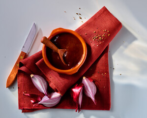 Chili Sauce in Terracotta Schale auf rostbrauner Serviette mit Messer und geschnittenen roten Zwiebeln geviertelt