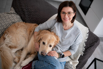 Happy Woman Hugging An Adorable Dog Relaxes On The Sofa At Home