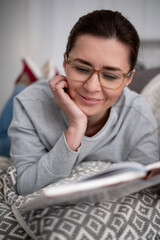 Happy Young Woman Reading An Interesting Book On The Sofa At Home