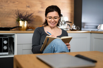 Young Woman Writing Notes In Notepad In Kitchen