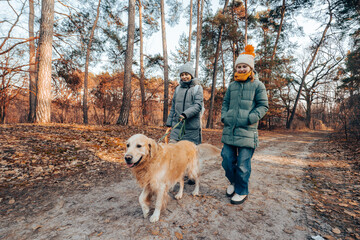 Mother With Little Daughter Walking With Golden Retriever Dog On A Leash In Autumn Park