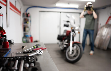 Man In Garage With Classic Motorcycle Wearing Protective Helmet