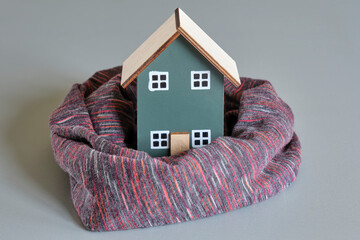 One miniature house in green with warm scarf on a grey background. Eco-friendly, energy neutral, energy price and house insulation concept.