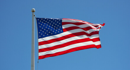 Fototapeta premium United States flag waving proudly against a clear blue sky, symbolizing patriotism and national identity.