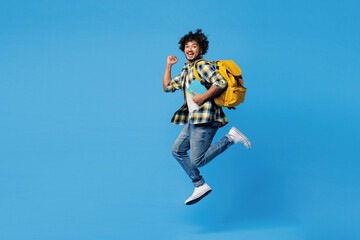 Full body young happy smart Indian boy student wear yellow casual clothes backpack bag hold books do winner gesture jump high isolated on plain blue background. High school university college concept.