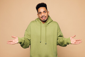 Young sad man of African American ethnicity wear green hoodie casual clothes shrugging shoulders...