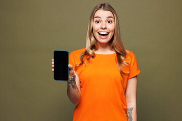 Young shocked surprised woman she wears orange t-shirt casual clothes hold in hand use mobile cell...