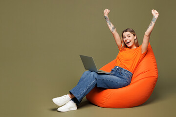 Full body young IT woman wears orange t-shirt casual clothes sit in bag chair hold use work on...