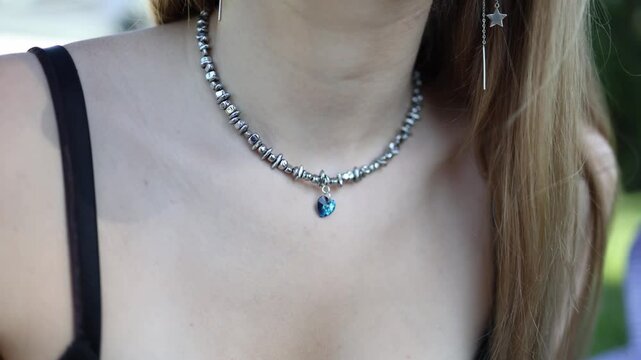 Closeup of elegant silver choker with shimmering blue heart pendant catching sunlight on bare skin paired with delicate star earring and soft natural tones