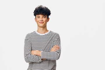young man wearing striped long sleeve shirt standing with crossed arms, smiling confidently against...